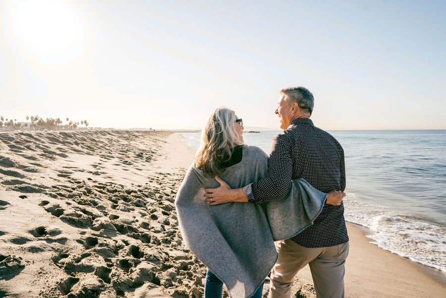 Smiling older couple wrapped in a blanket, walking along the beach